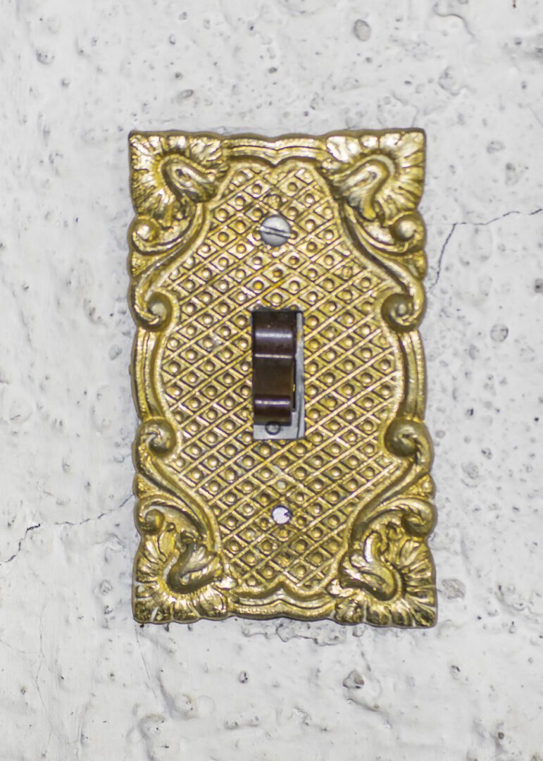 Ornate brass light switch plate with a toggle switch on marble wall.
